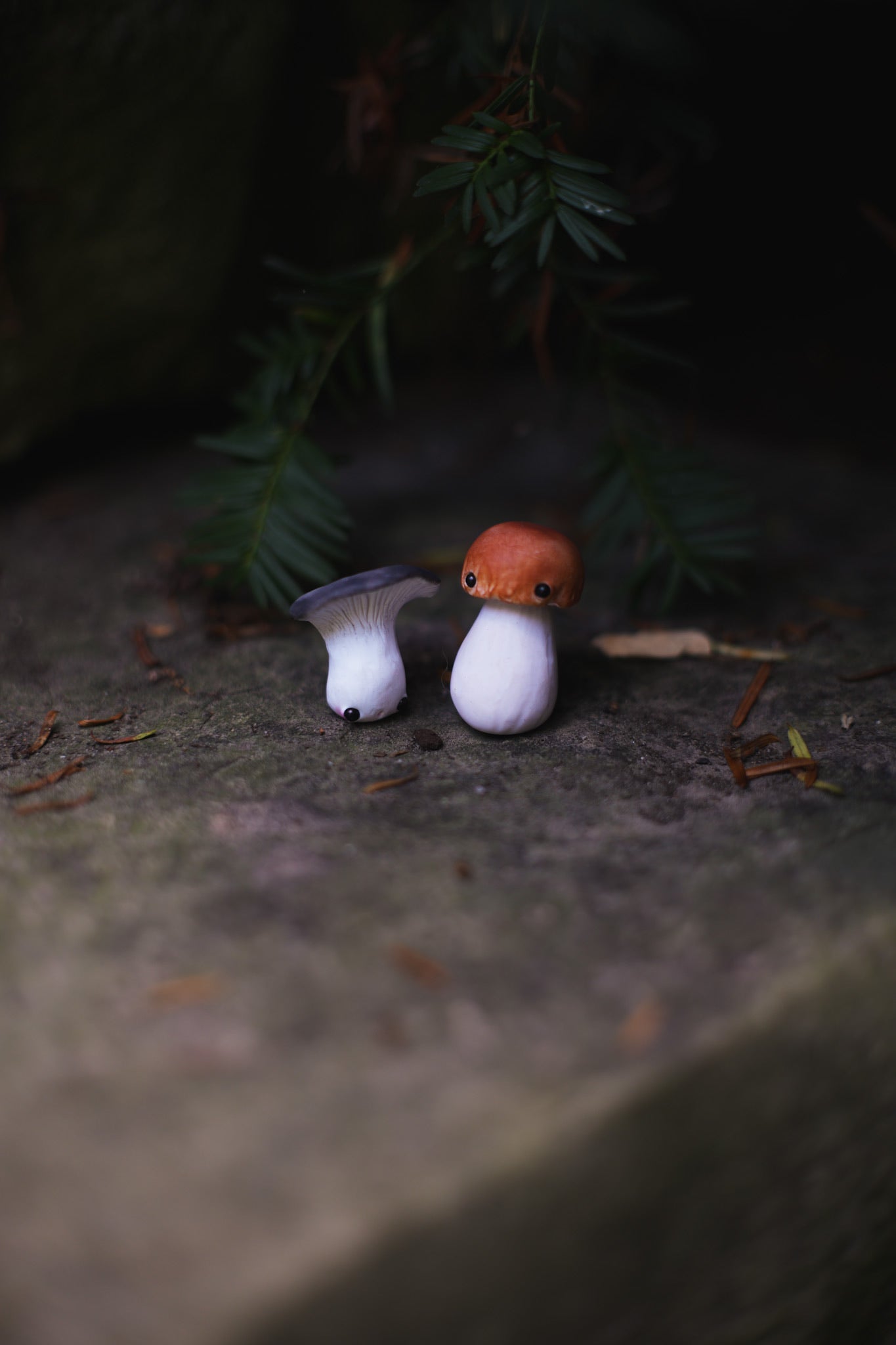 Two small mushroom figurines on a dark surface with greenery in the background