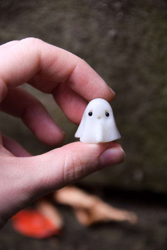 Hand holding a small white ghost figurine against a blurred natural background